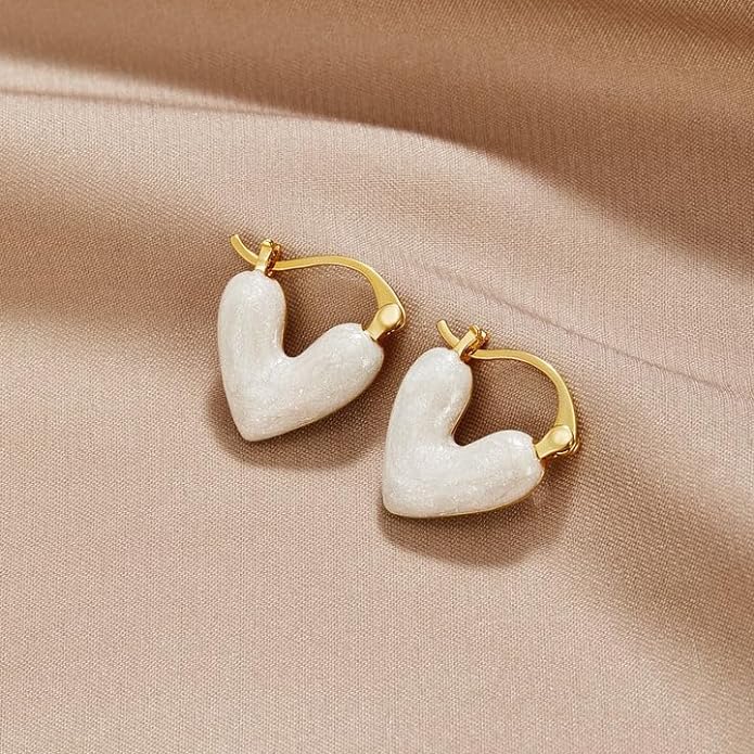 White heart-shaped earrings on beige background, perfect for adding a touch of elegance to any outfit.