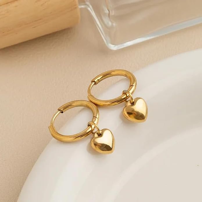 Two gold heart-shaped hoop earrings on a plate.