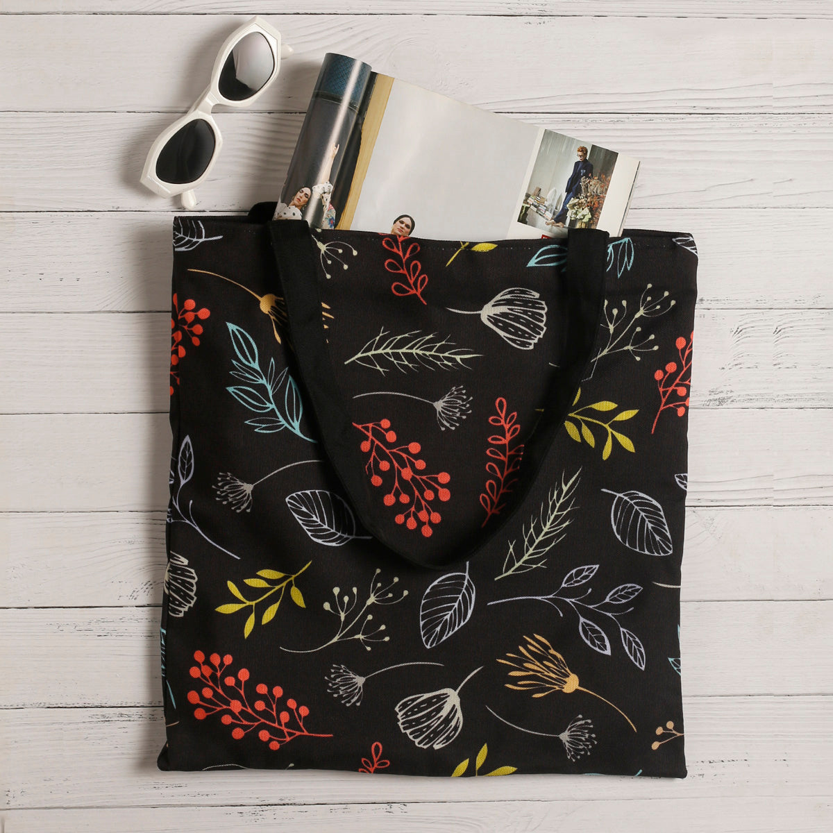 A black tote bag adorned with colorful leaves and flowers.